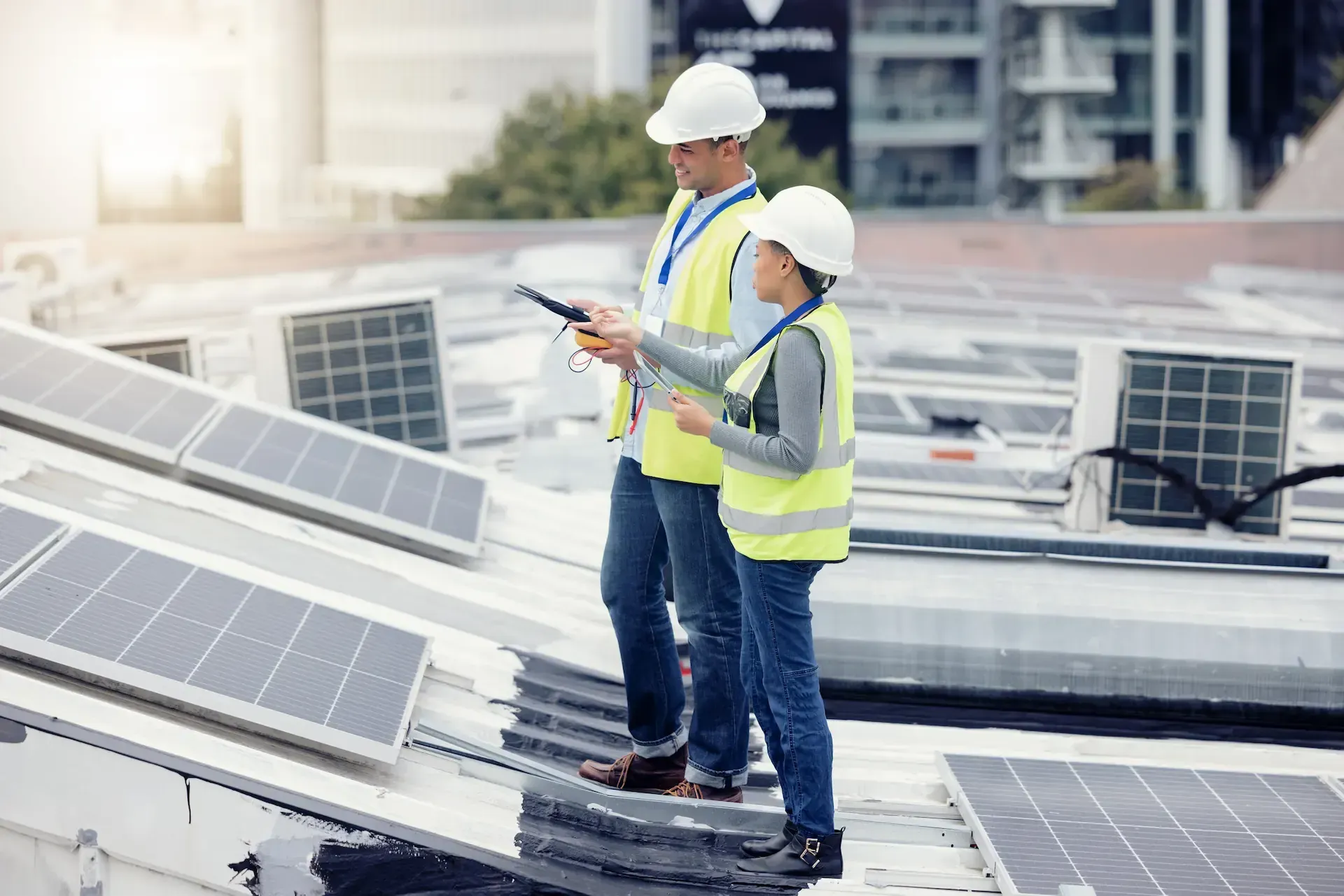 Dos personas con cascos y chalecos inspeccionan paneles solares en un tejado.