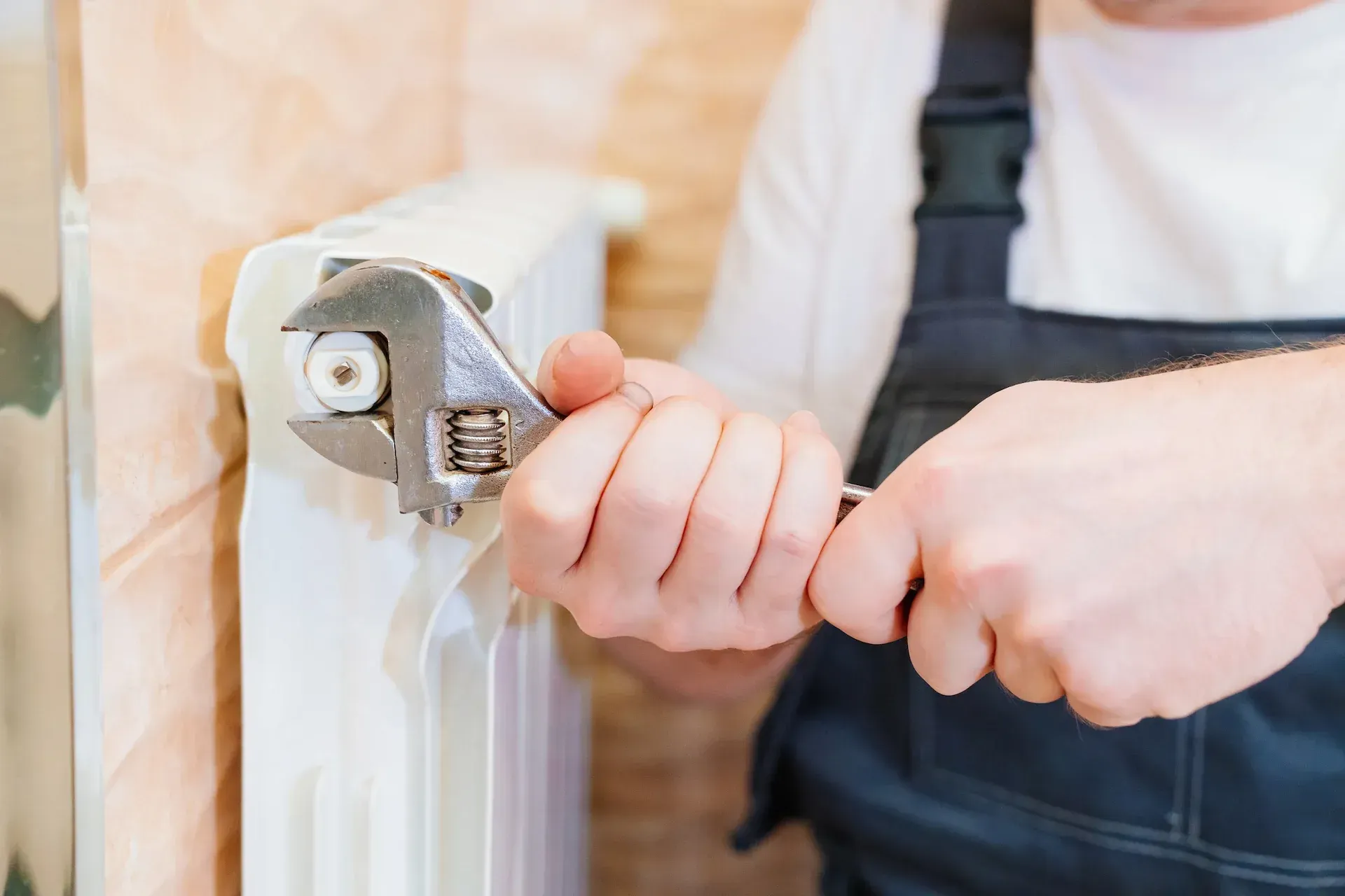 Una persona que utiliza una llave inglesa para trabajar en un radiador blanco.