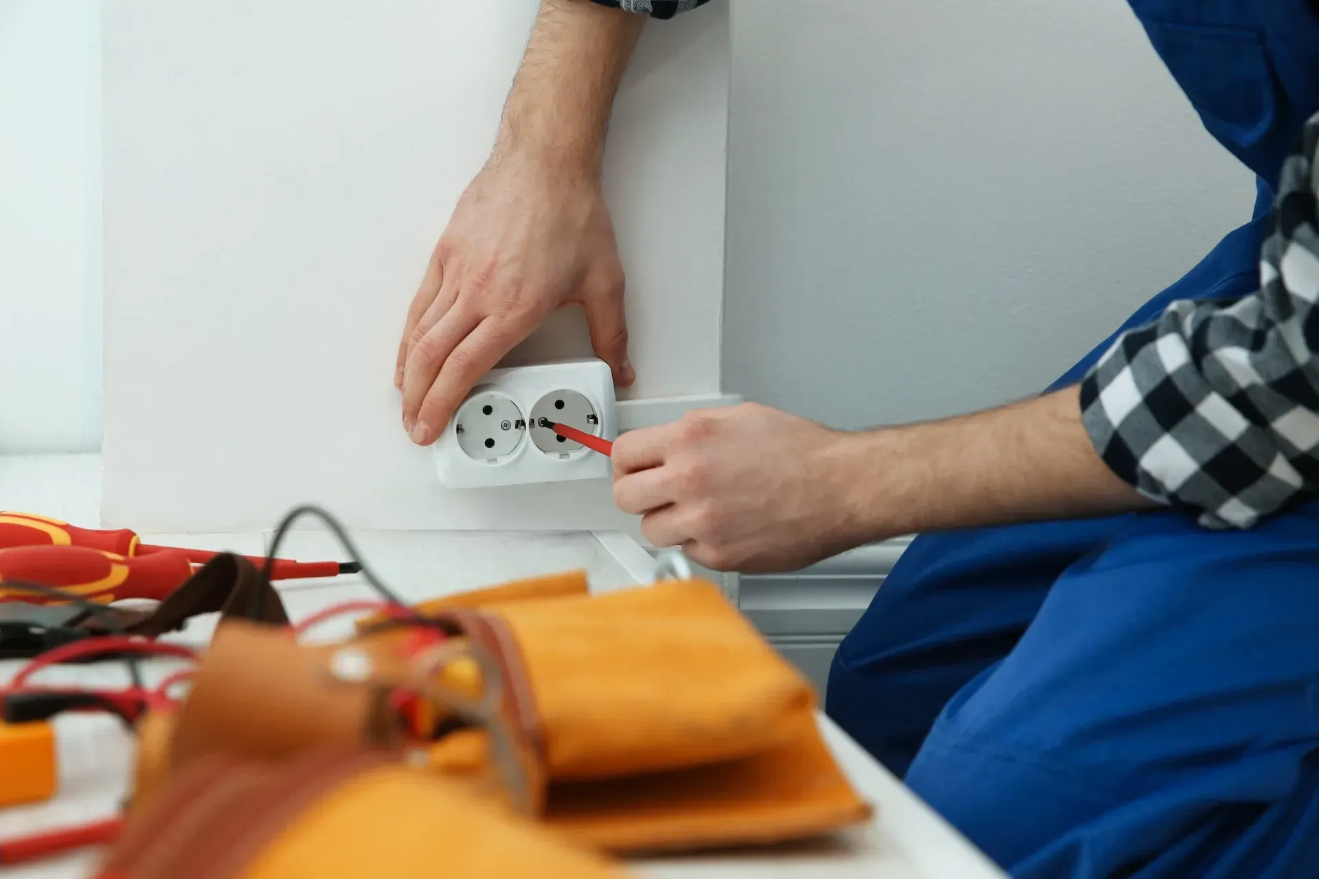 Electricista instalando un enchufe con un destornillador. Herramientas y cinturón de trabajo a la vista.