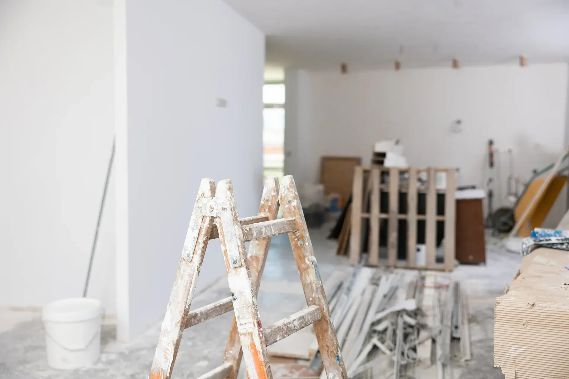 Interior de una habitación en reforma con escalera, palets de madera y herramientas.