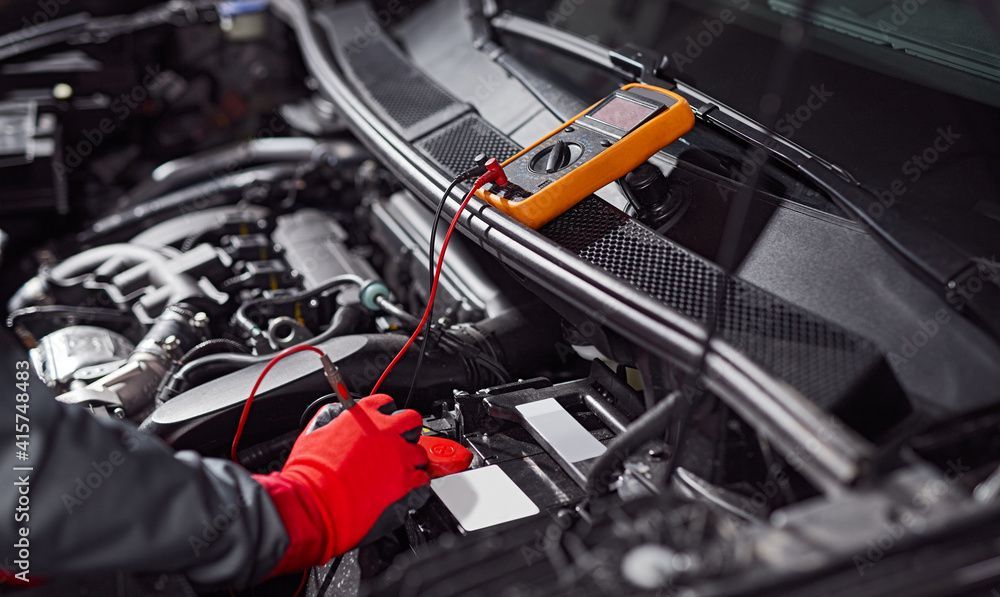 Ein Mechaniker arbeitet mit einem Multimeter an einem Automotor.
