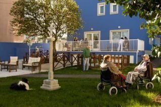 Un grupo de personas está sentado en el césped frente a un edificio azul.