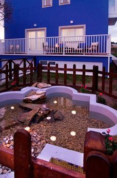 Una casa azul con una valla de madera y un estanque delante de ella.