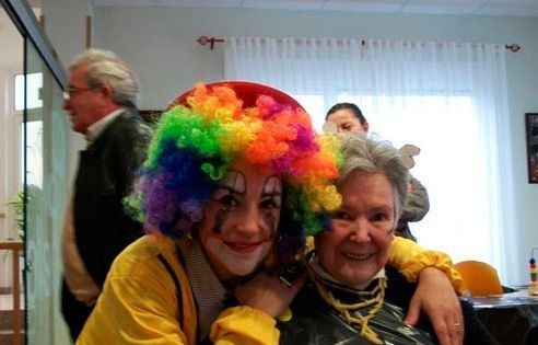 Una niña con una peluca de payaso abraza a una mujer mayor.