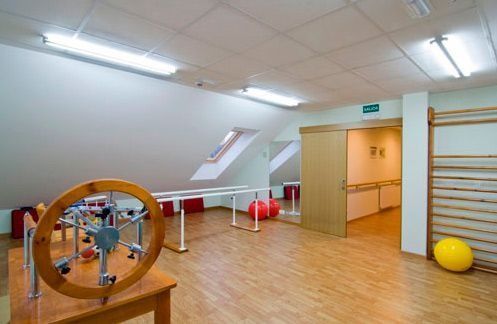 Un gimnasio con suelo de madera, aparatos de ejercicio, una mesa y un espejo.