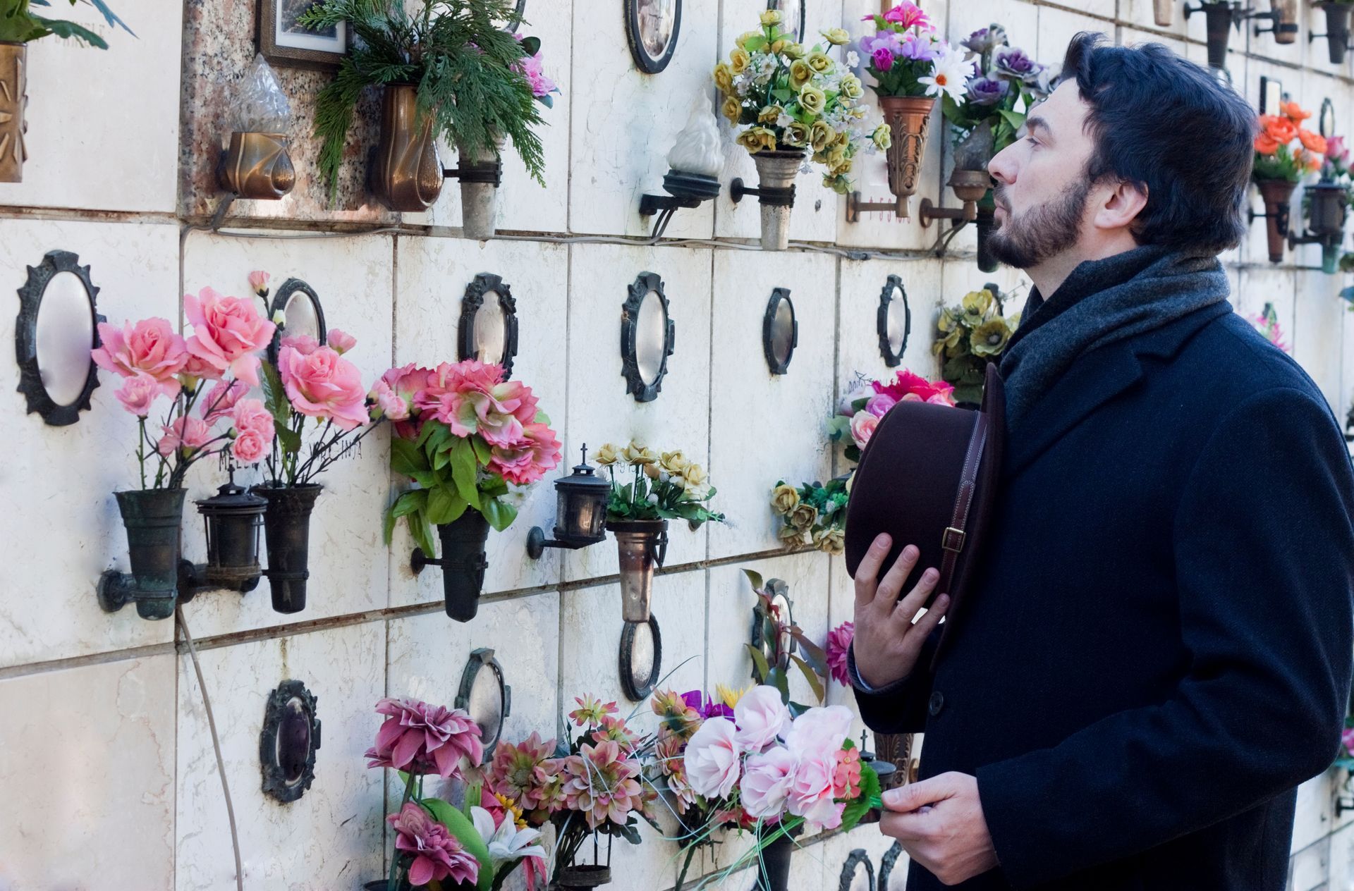 Un homme tenant son chapeau en face d’un mur de fleurs