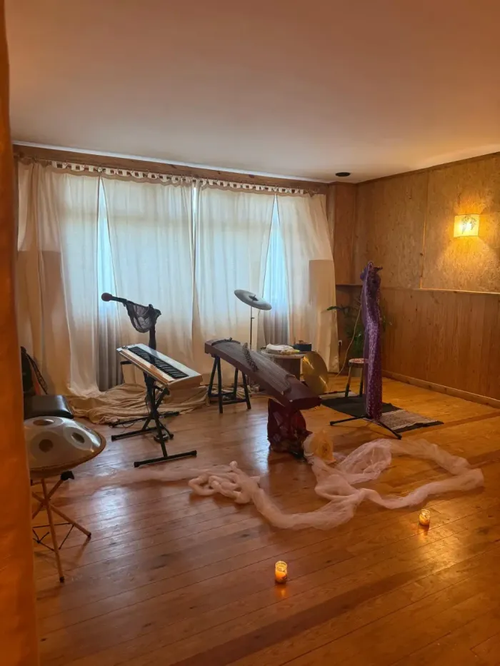 Sala de masajes con camillas de terapia, suelo de madera, cortinas suaves y una pequeña vela en el suelo.