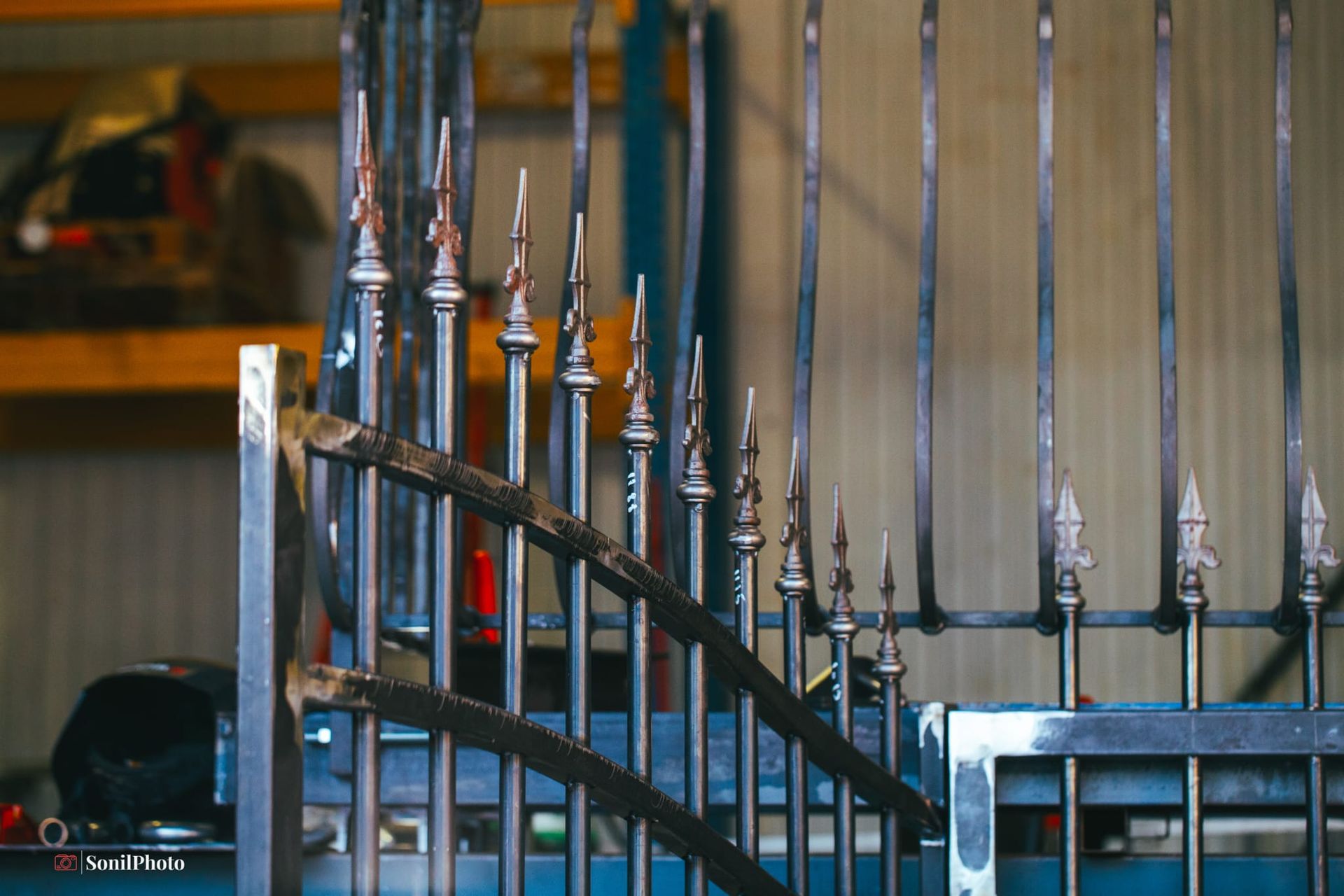 Portail métallique en construction avec des sommets décoratifs en forme de lance dans un atelier.