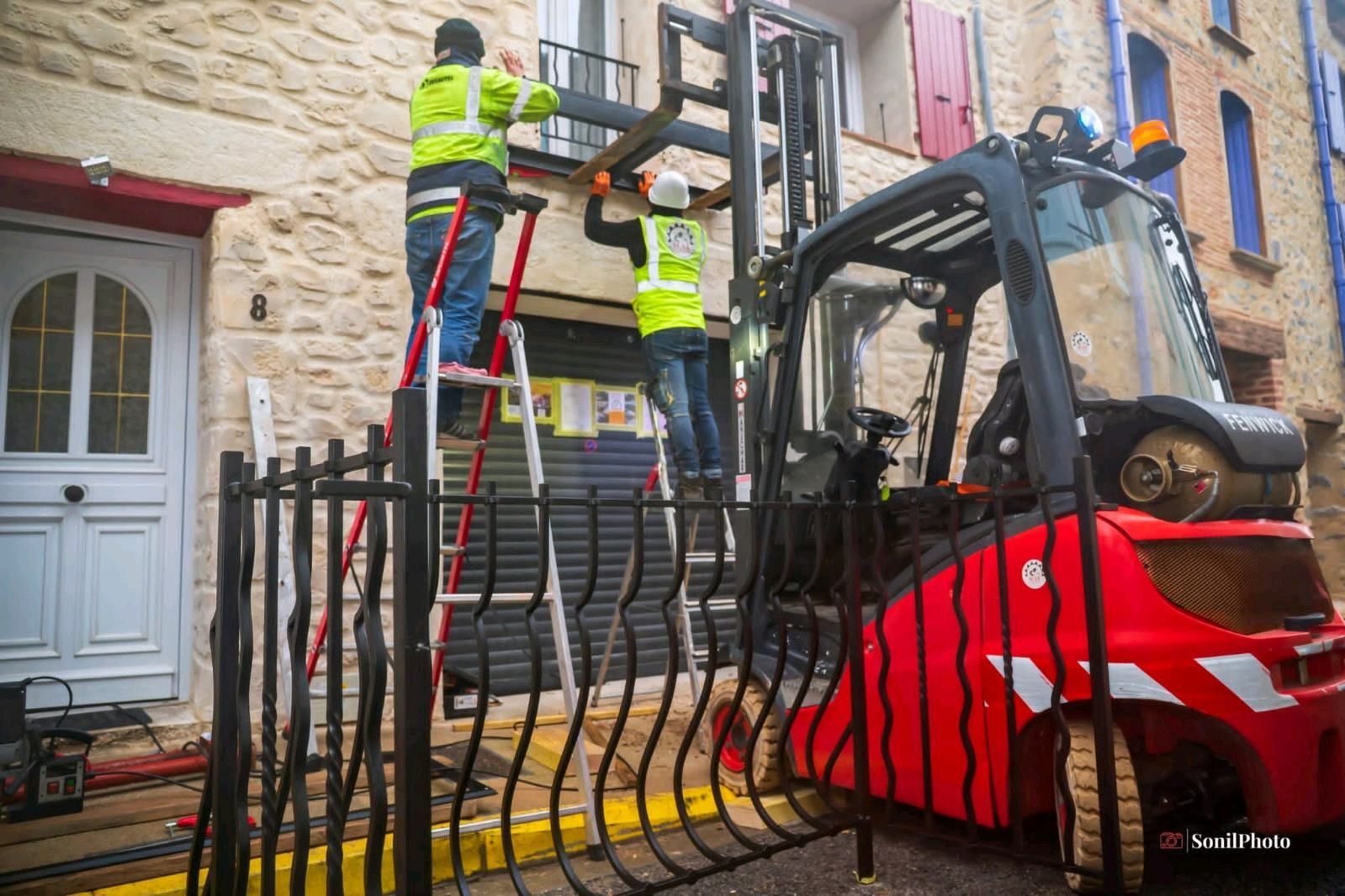 Des ouvriers sur une échelle et un chariot élévateur installent des garnitures de façade sur un bâtiment.