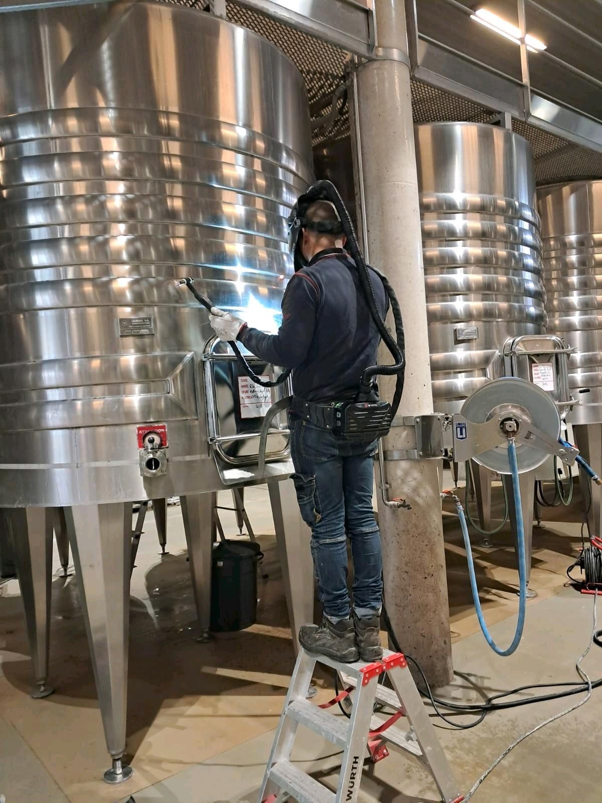 Soudeur en équipement de protection travaillant sur un grand réservoir en acier inoxydable.