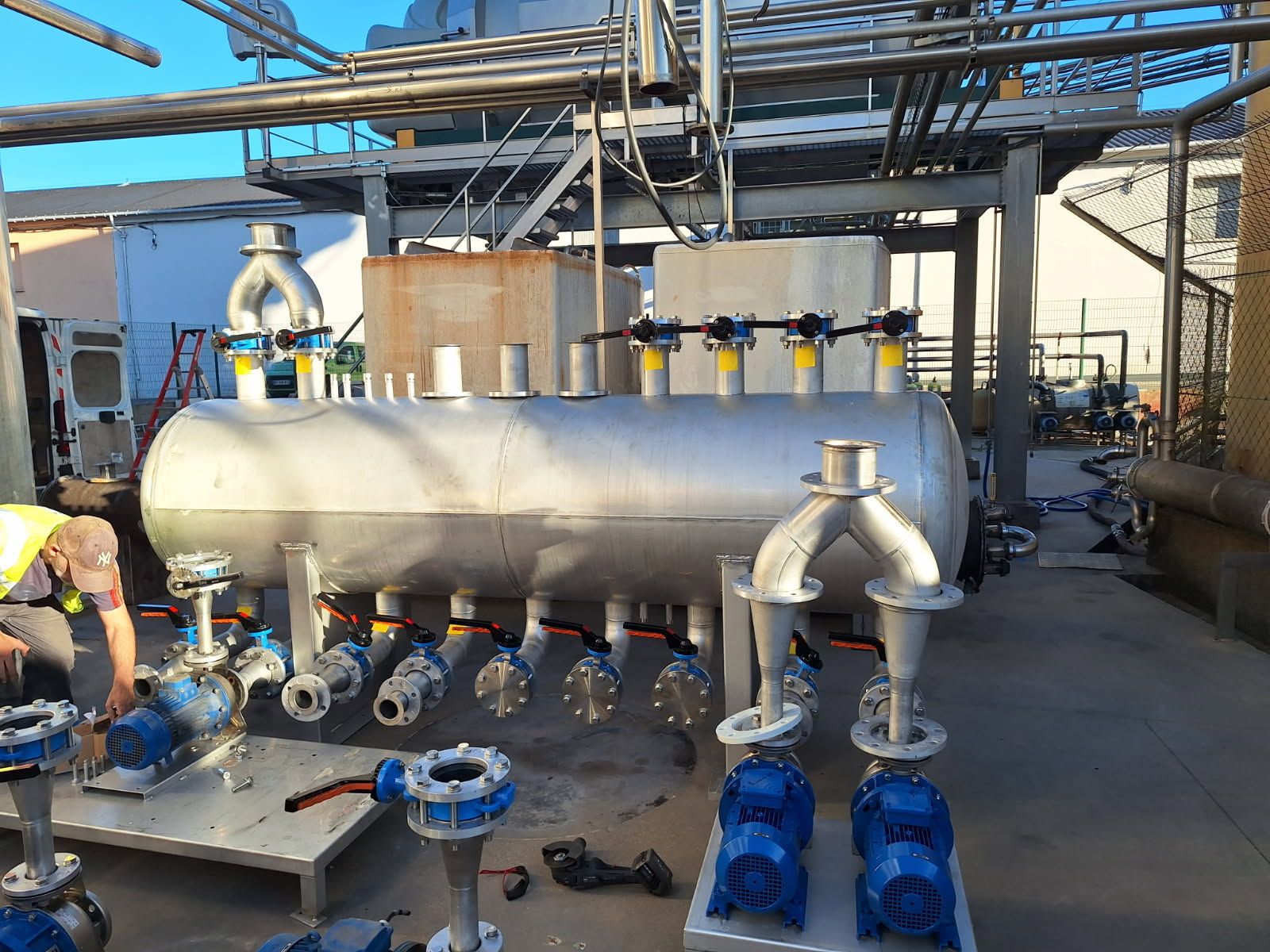 Grand réservoir industriel avec divers tuyaux, pompes et vannes, probablement pour le traitement de liquides.