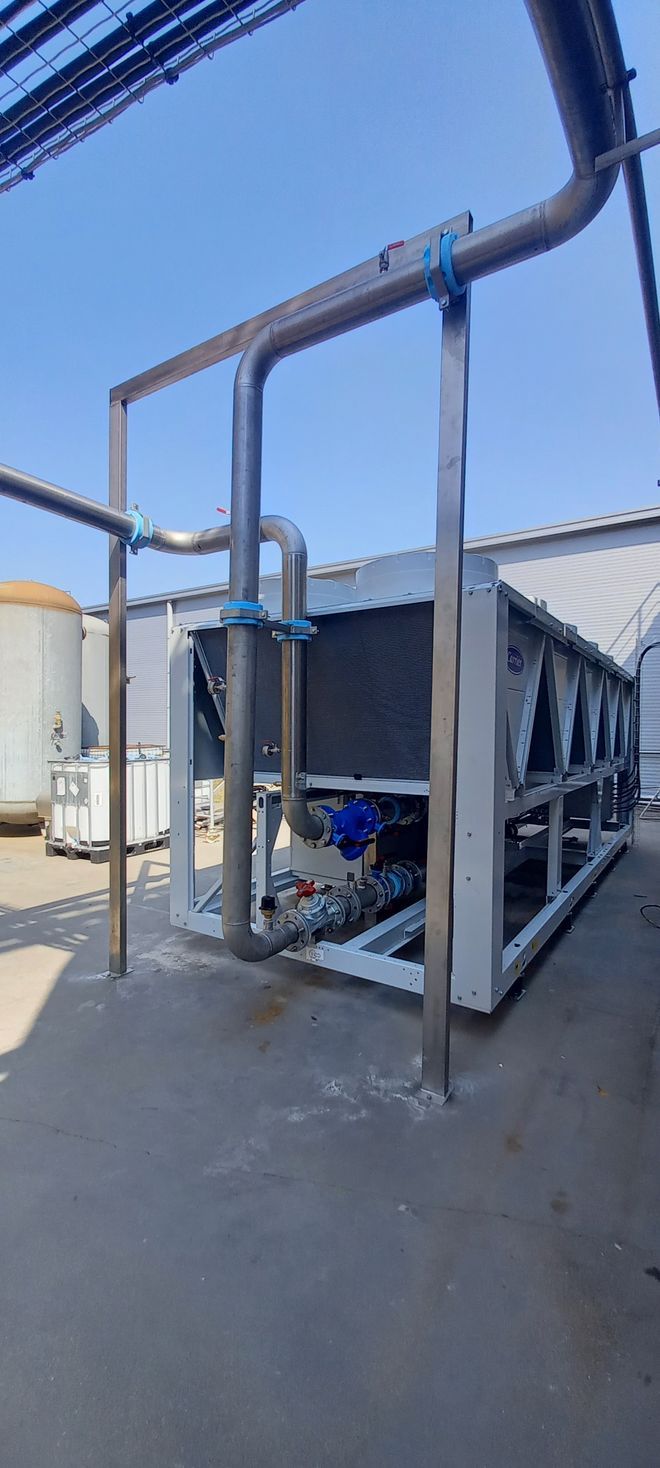 Une unité de refroidissement industrielle avec tuyauterie, à l'extérieur contre un ciel bleu.