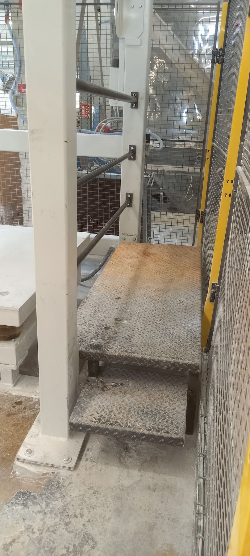 Deux marches en métal, un pilier blanc et une plate-forme en métal à l'intérieur d'une usine.
