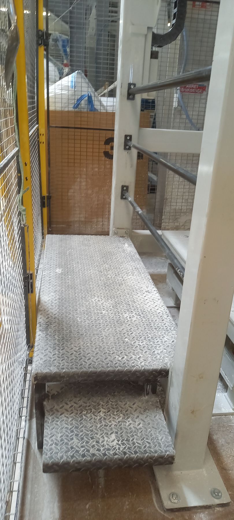 Escalier et passerelle métalliques près des machines, en milieu industriel. Barrière de sécurité jaune à gauche.