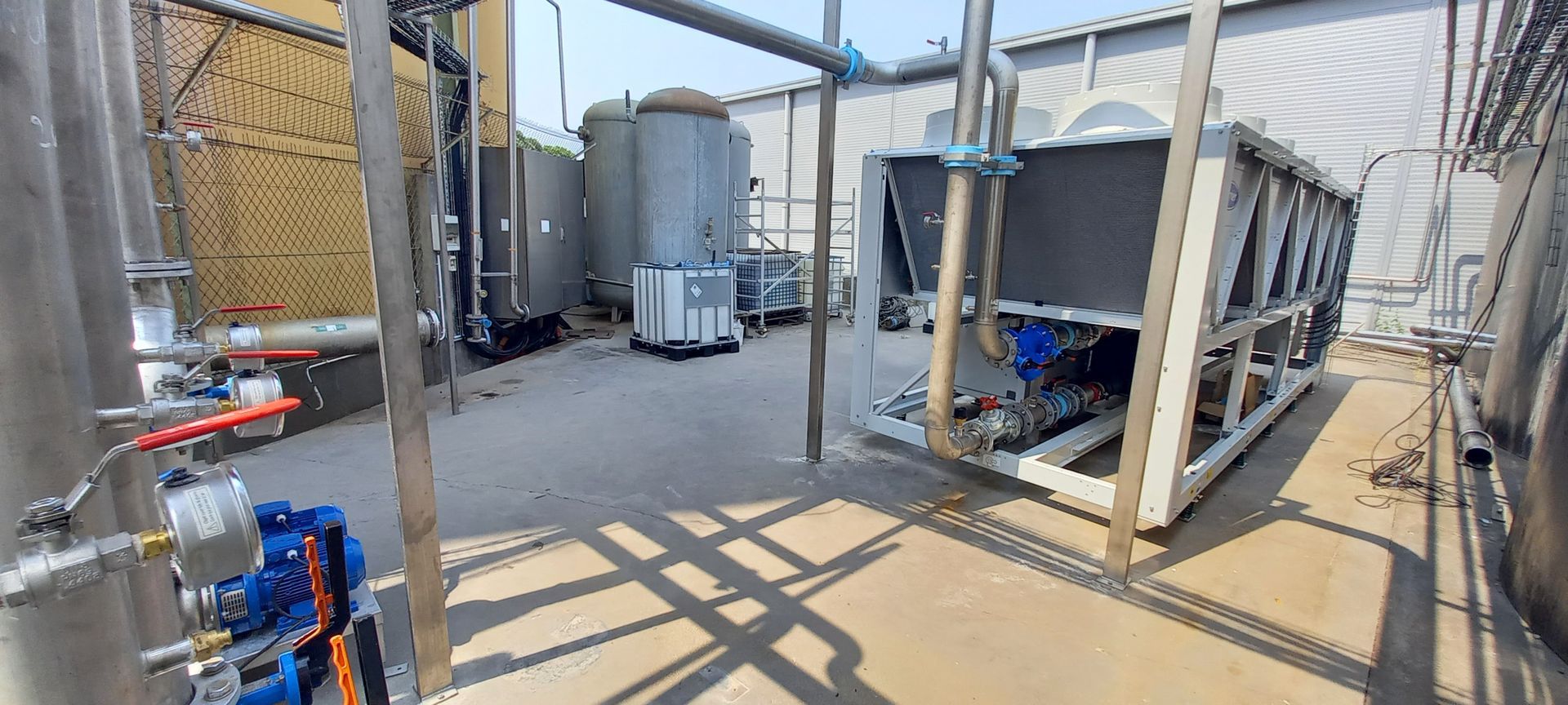 Équipements industriels extérieurs : réservoirs et grandes unités de refroidissement, sur une surface en béton.