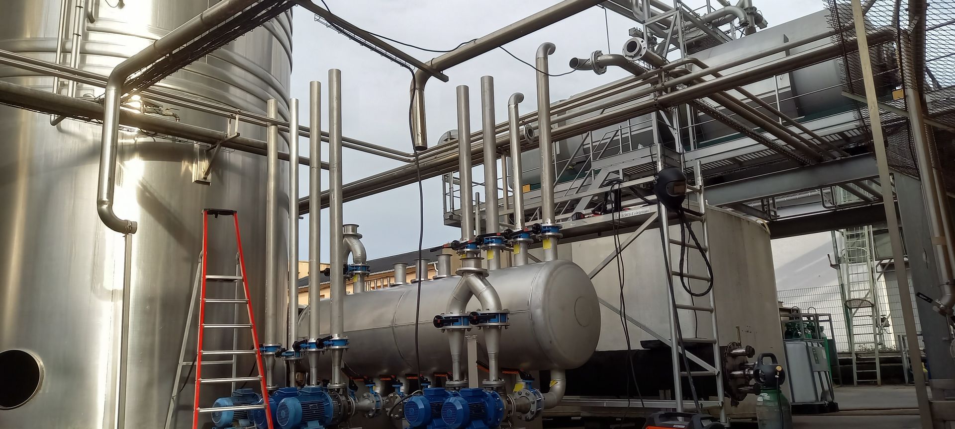 Installation industrielle avec de grands réservoirs métalliques, des tuyaux et une échelle contre l'un des réservoirs.