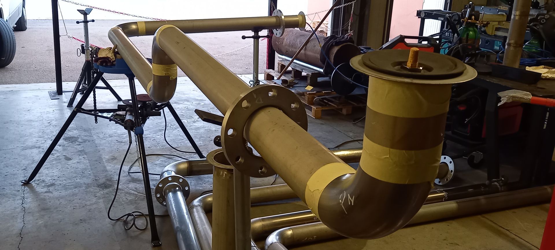 Tubes avec raccords à brides, installés dans un atelier avec divers équipements en arrière-plan.