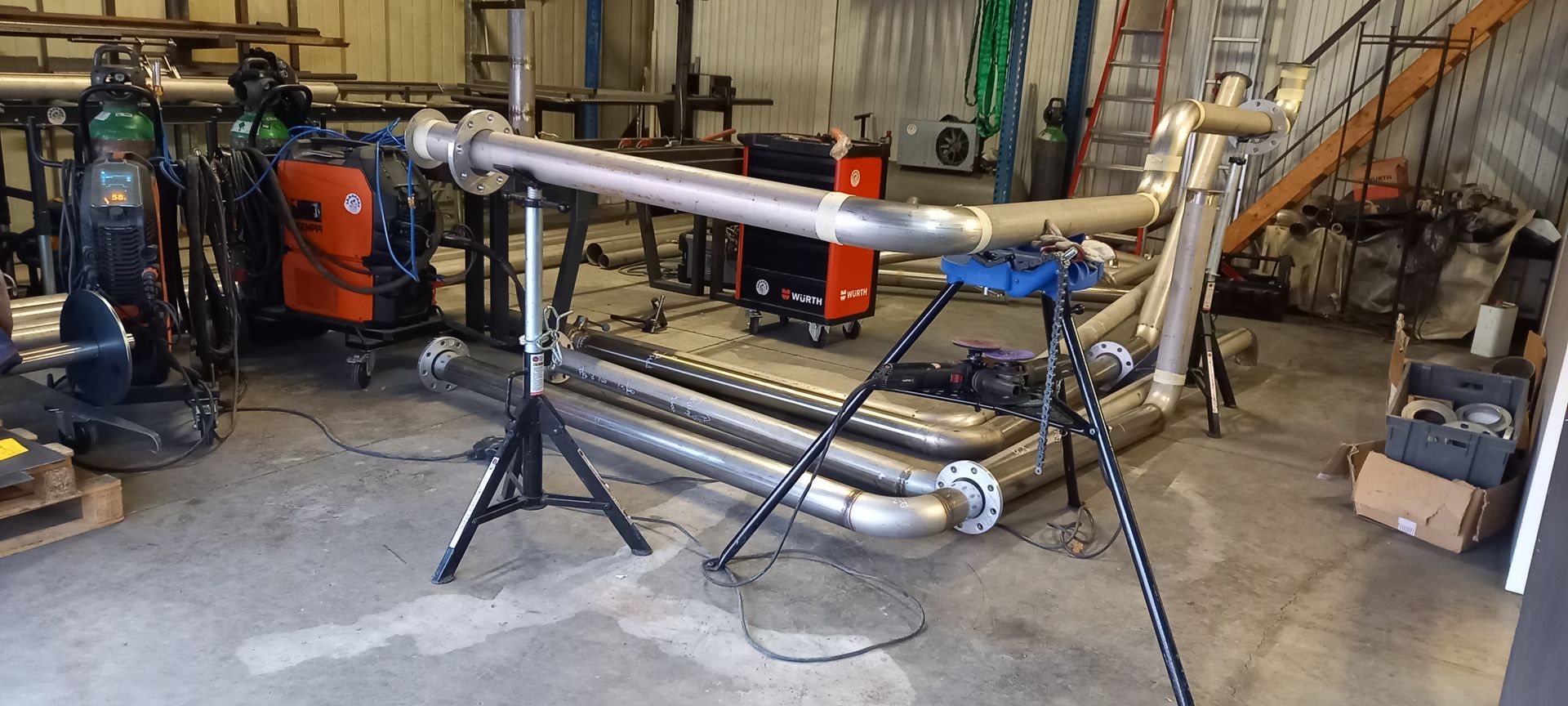 Tubes métalliques dans un atelier, soutenus par des trépieds. Équipement et outils de soudage en arrière-plan.