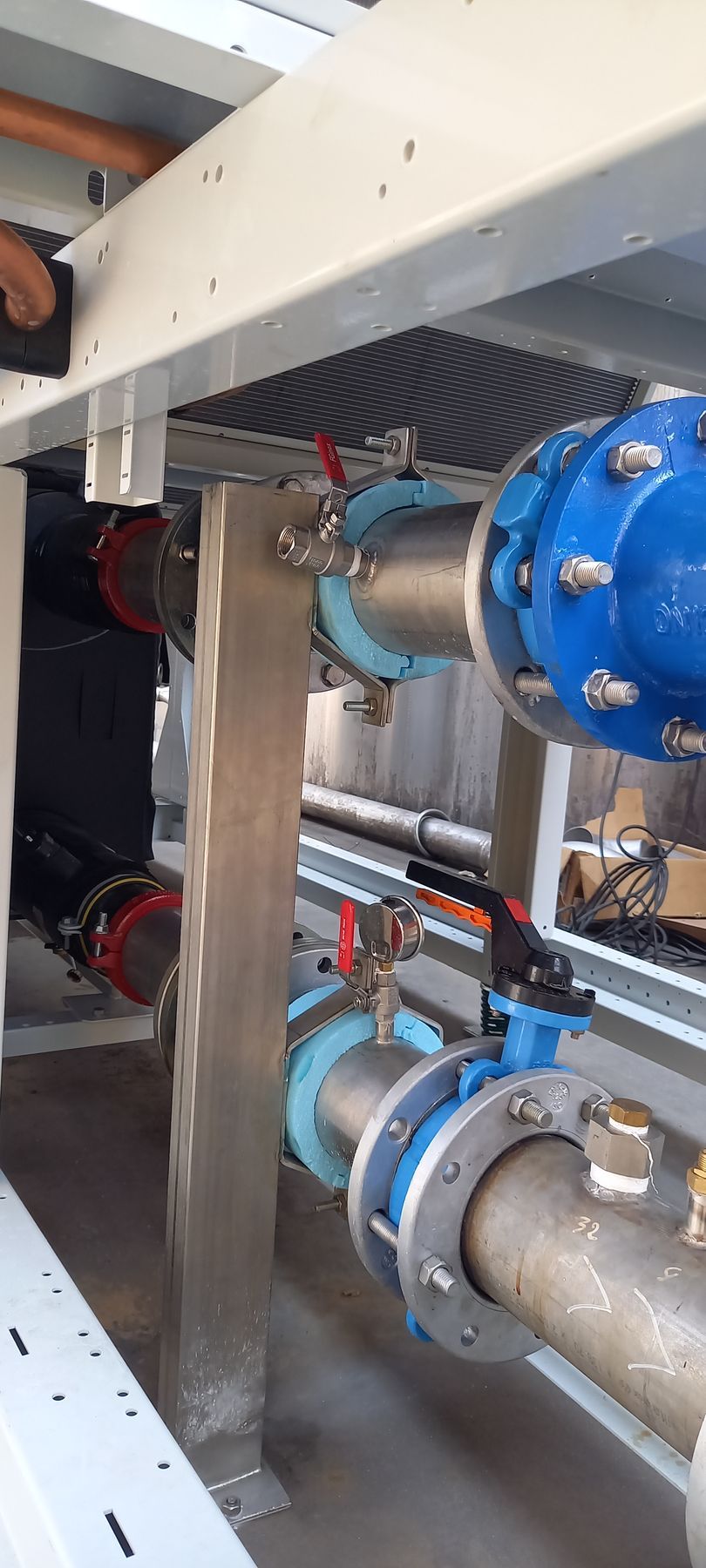 Tuyaux avec vannes bleues et rouges, reliés par des brides, soutenus par une structure métallique, cadre industriel.
