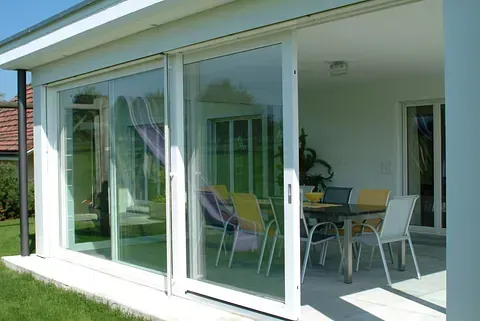 Hay una mesa y sillas afuera de una casa con puertas corredizas de vidrio.