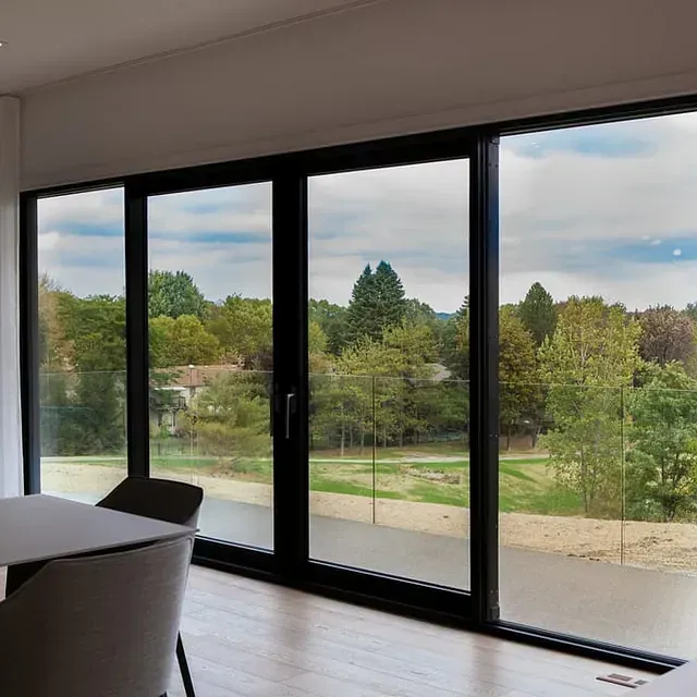 Un comedor con mesa y sillas y un gran ventanal con vista a un bosque.