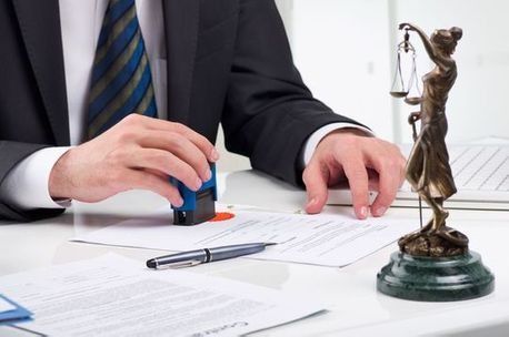 Un hombre con traje y corbata está sellando un documento junto a una estatua de la justicia.