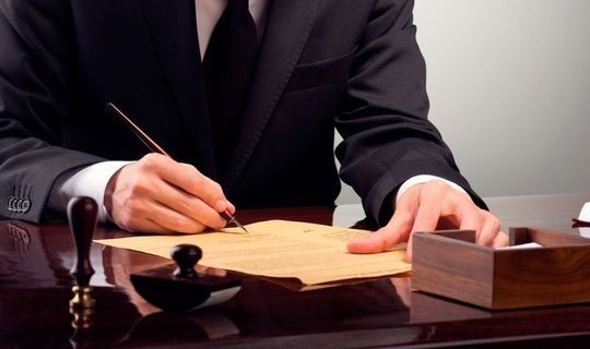 Un hombre con traje está escribiendo en un trozo de papel con un bolígrafo.