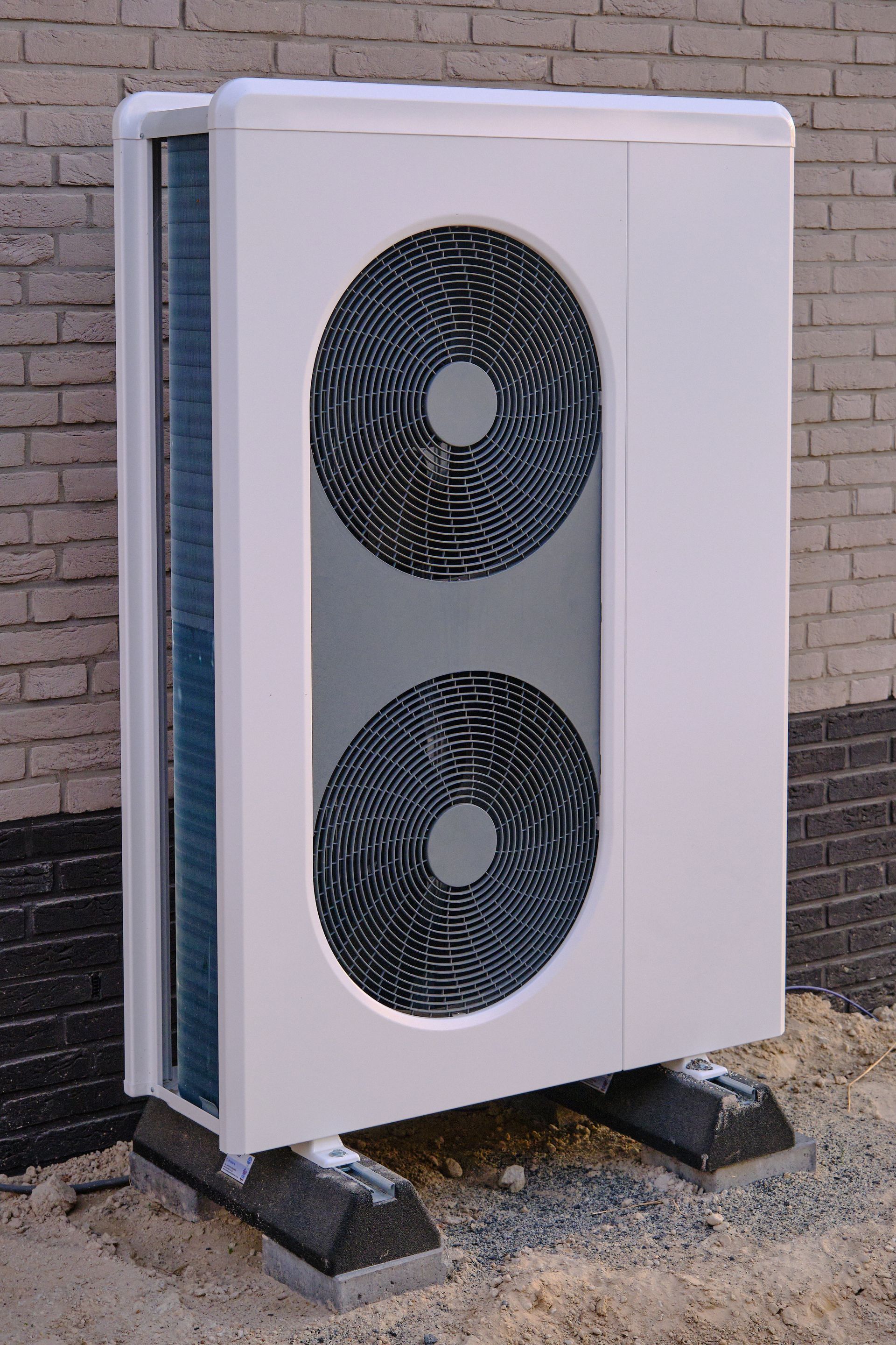 Une pompe à chaleur air-air, montée sur deux supports en caoutchouc, contre un mur de briques.