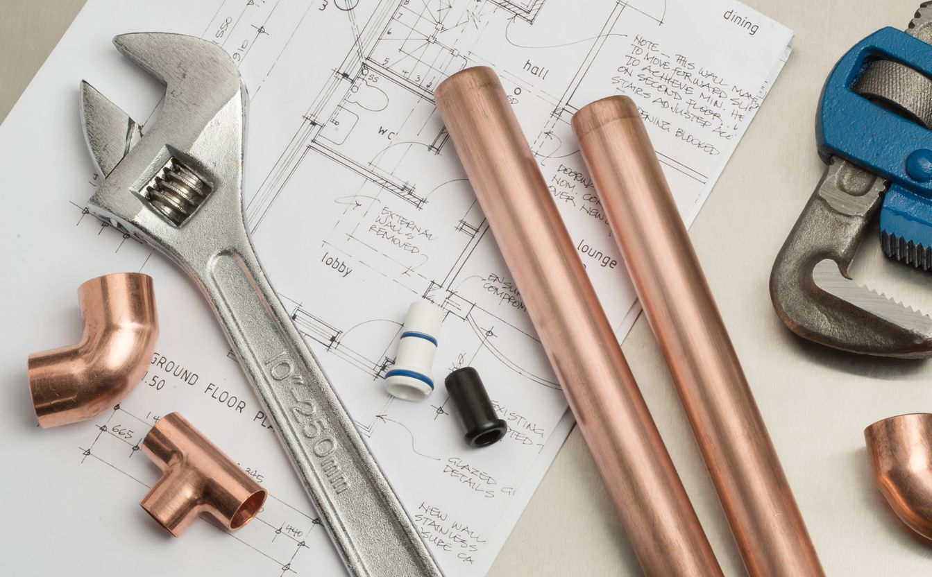 Des tuyaux de cuivre, divers raccords de plomberie et des outils disposés sur des plans de construction.