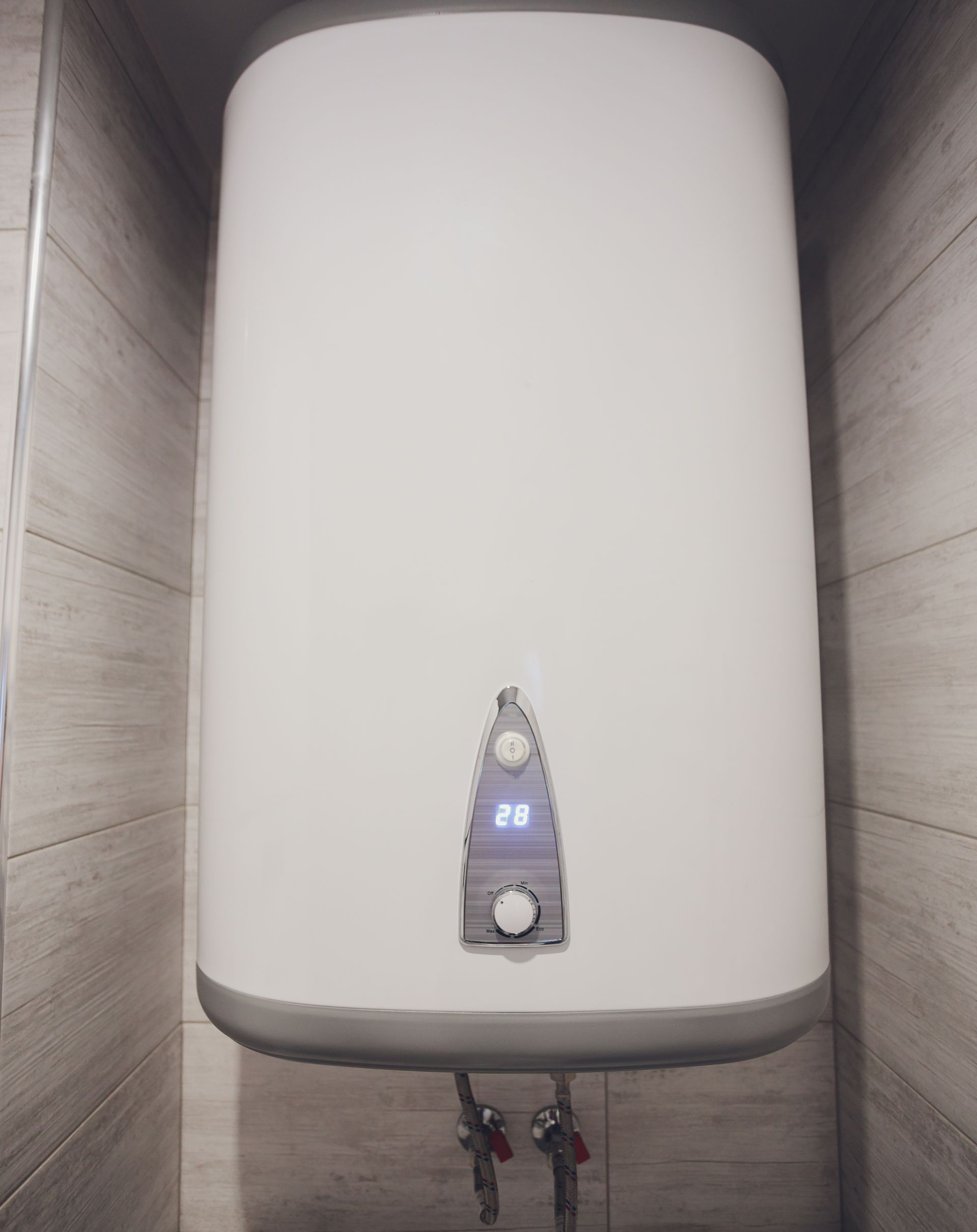 Un chauffe-eau électrique avec affichage numérique de la température réglé à 28 degrés, fixé sur un mur carrelé.