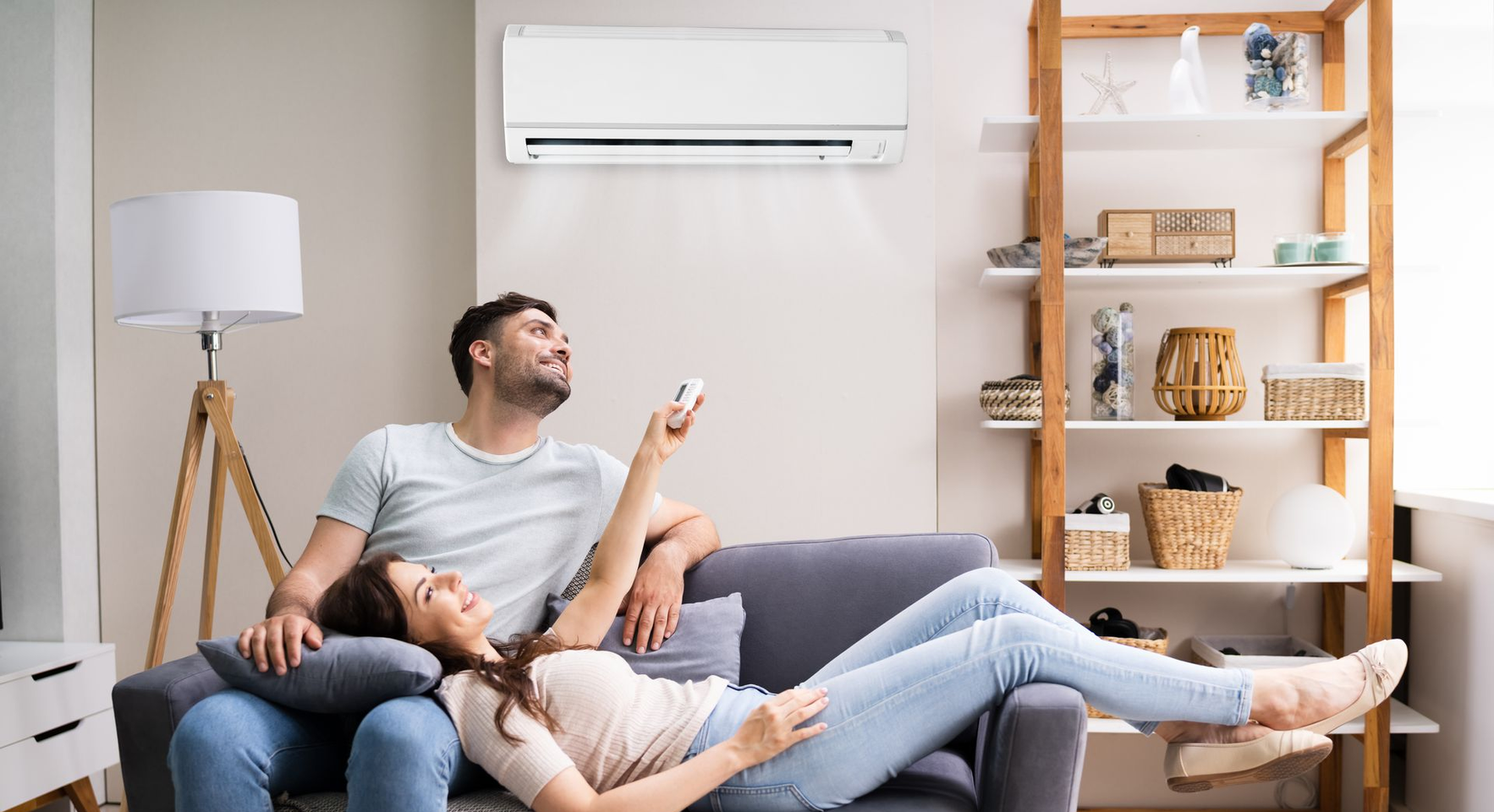 Un couple se détend sur un canapé dans un salon, utilisant une télécommande pour régler un climatiseur mural.