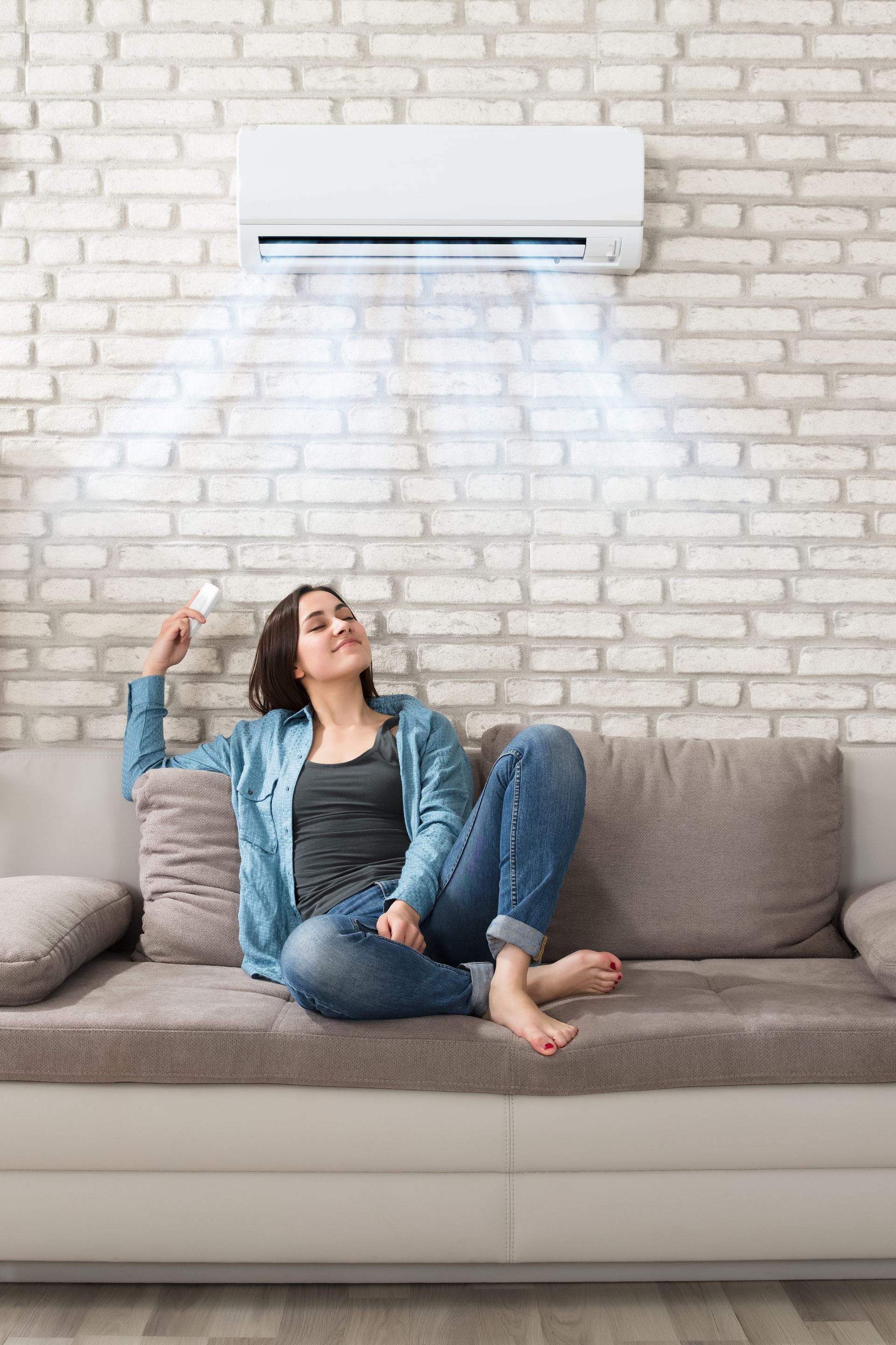 Une personne est assise sur un canapé, se détendant sous un climatiseur mural qui souffle de l'air frais contre un mur de briques.