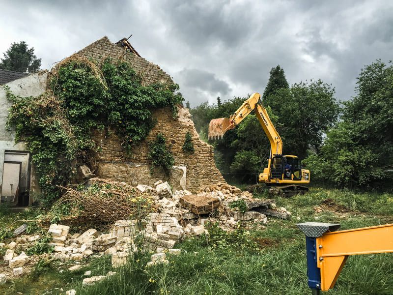 Ein gelber Bagger zerstört auf einem Feld ein Gebäude.