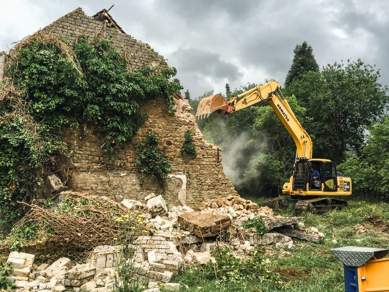 Ein gelber Bagger zerstört ein Backsteingebäude.