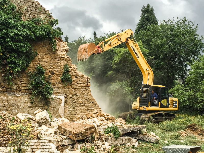 Ein gelber Bagger zerstört eine Steinmauer.