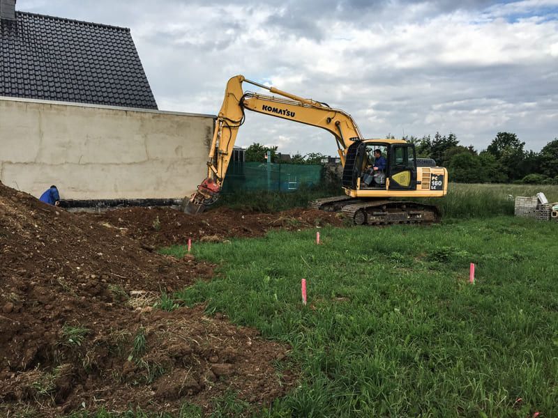 Ein gelber Bagger gräbt ein Loch in eine Wiese.