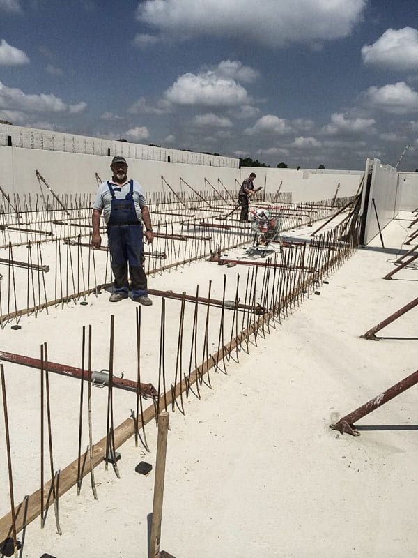 Ein Mann im blauen Overall steht mitten auf einer Baustelle.