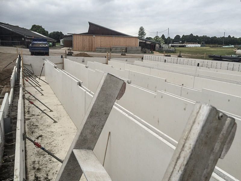 Auf einem Feld wird eine Betonmauer gebaut, im Hintergrund ist ein Gebäude zu sehen.
