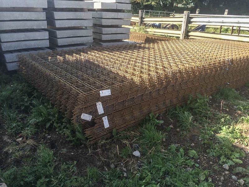 Ein Stapel Maschendraht liegt im Gras neben einem Zaun.