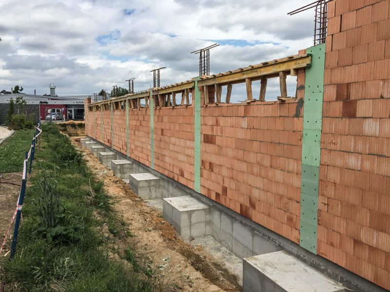 Auf einem Feld wird eine große Backsteinmauer gebaut.
