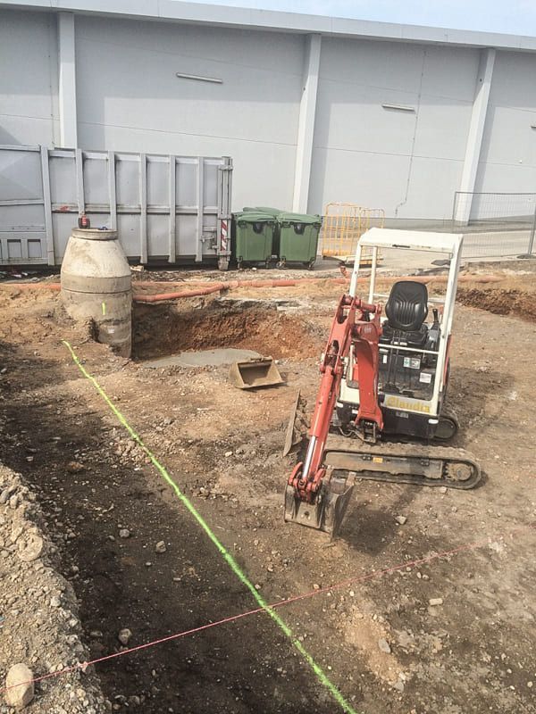 Ein kleiner Bagger steht auf einem Feld vor einem großen Gebäude.