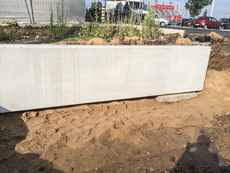 Ein großer Blumenkasten aus Beton steht im Dreck in der Nähe eines Parkplatzes.