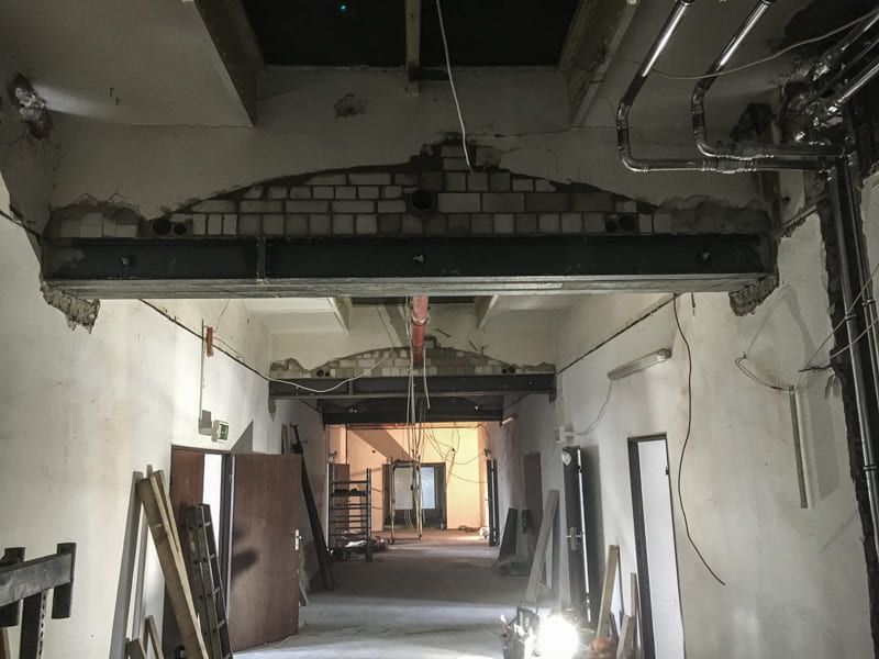 Ein langer Flur in einem im Bau befindlichen Gebäude mit einer Ziegelwand und Rohren, die von der Decke hängen.