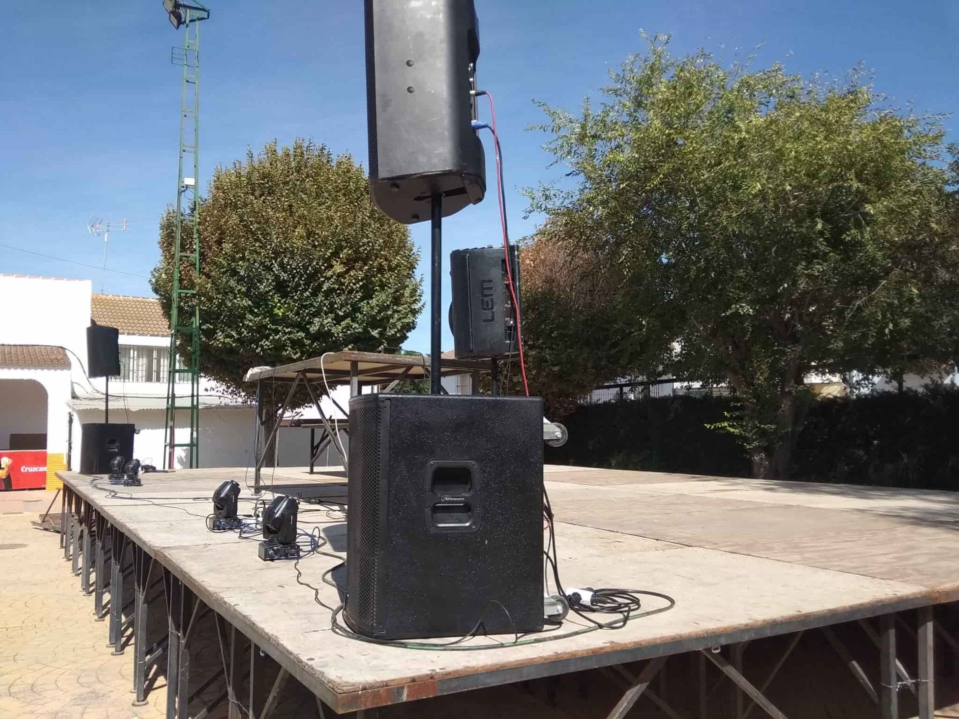 Un sistema de sonido negro cuelga sobre un escenario con alfombra roja, estructuras ornamentadas y un fondo de ciudad.