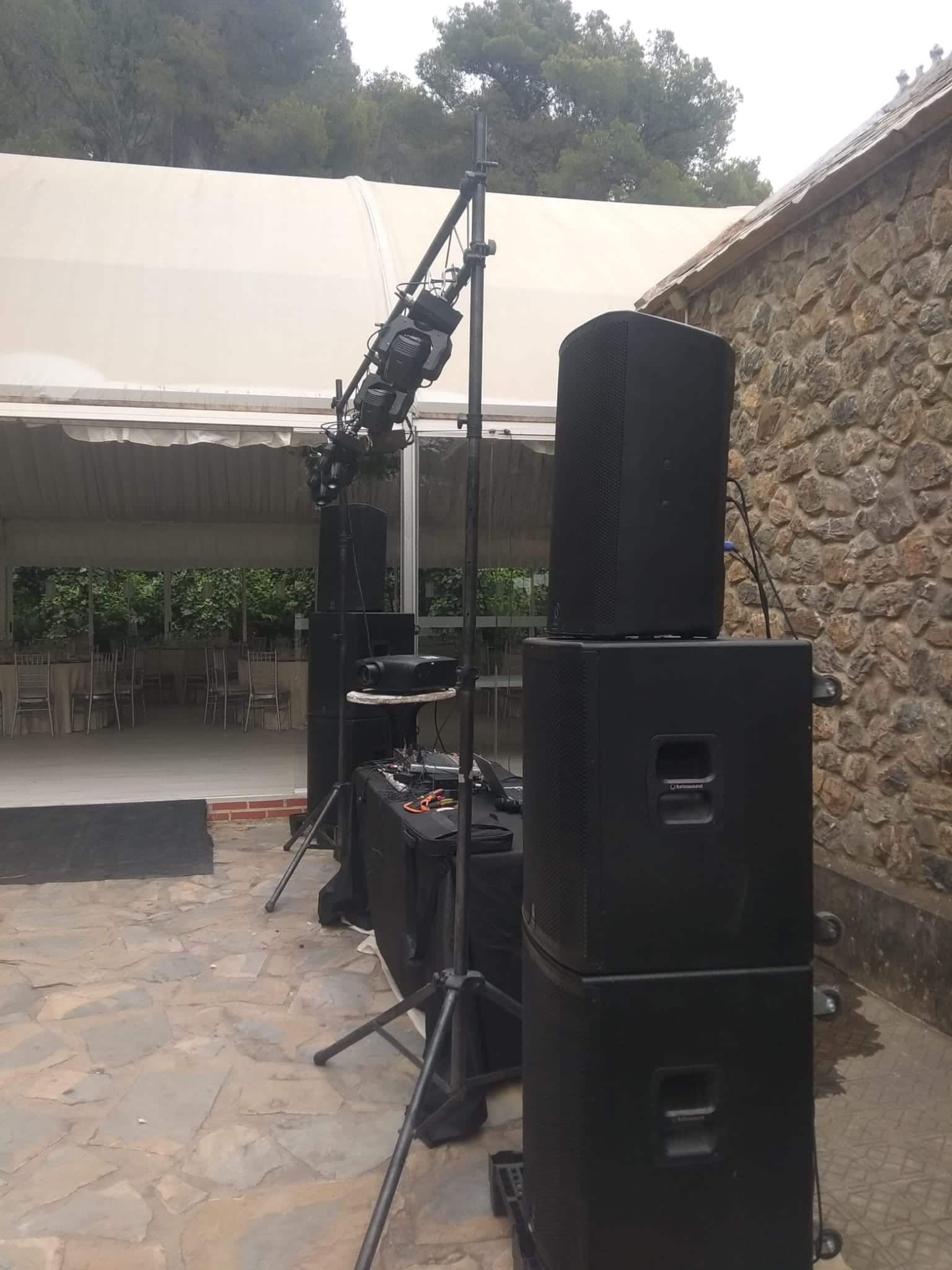 Configuración de DJ con altavoces, luces y equipos en un patio al aire libre.