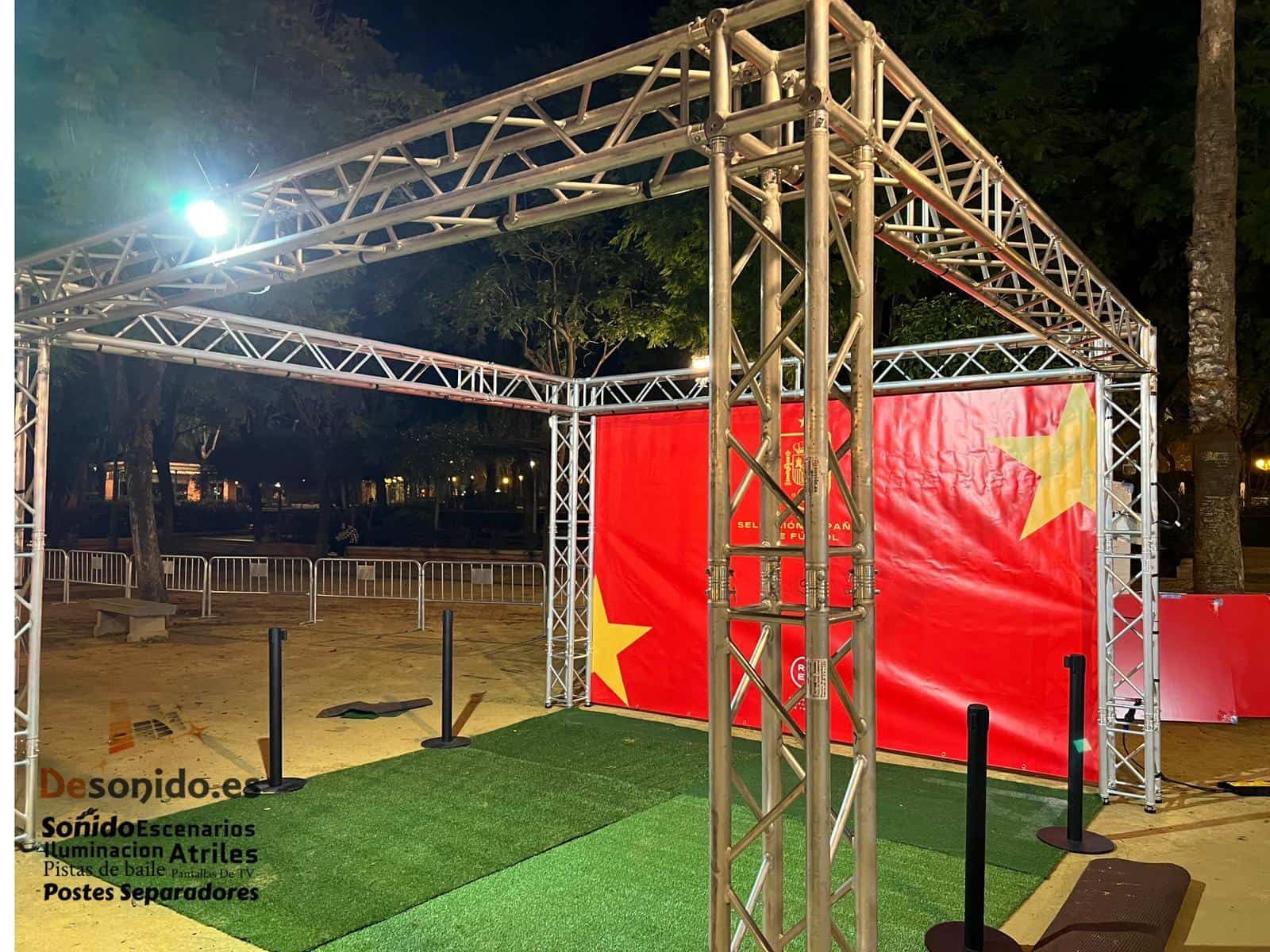 Estructura metálica con bandera roja y amarilla sobre césped verde. Exterior oscuro.