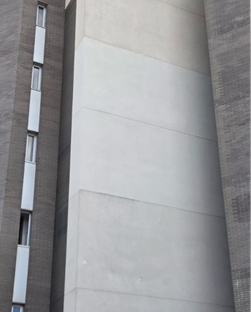 Fachada de edificio alto de hormigón gris con estrechas franjas verticales de ventanas y un panel de pared blanco liso.