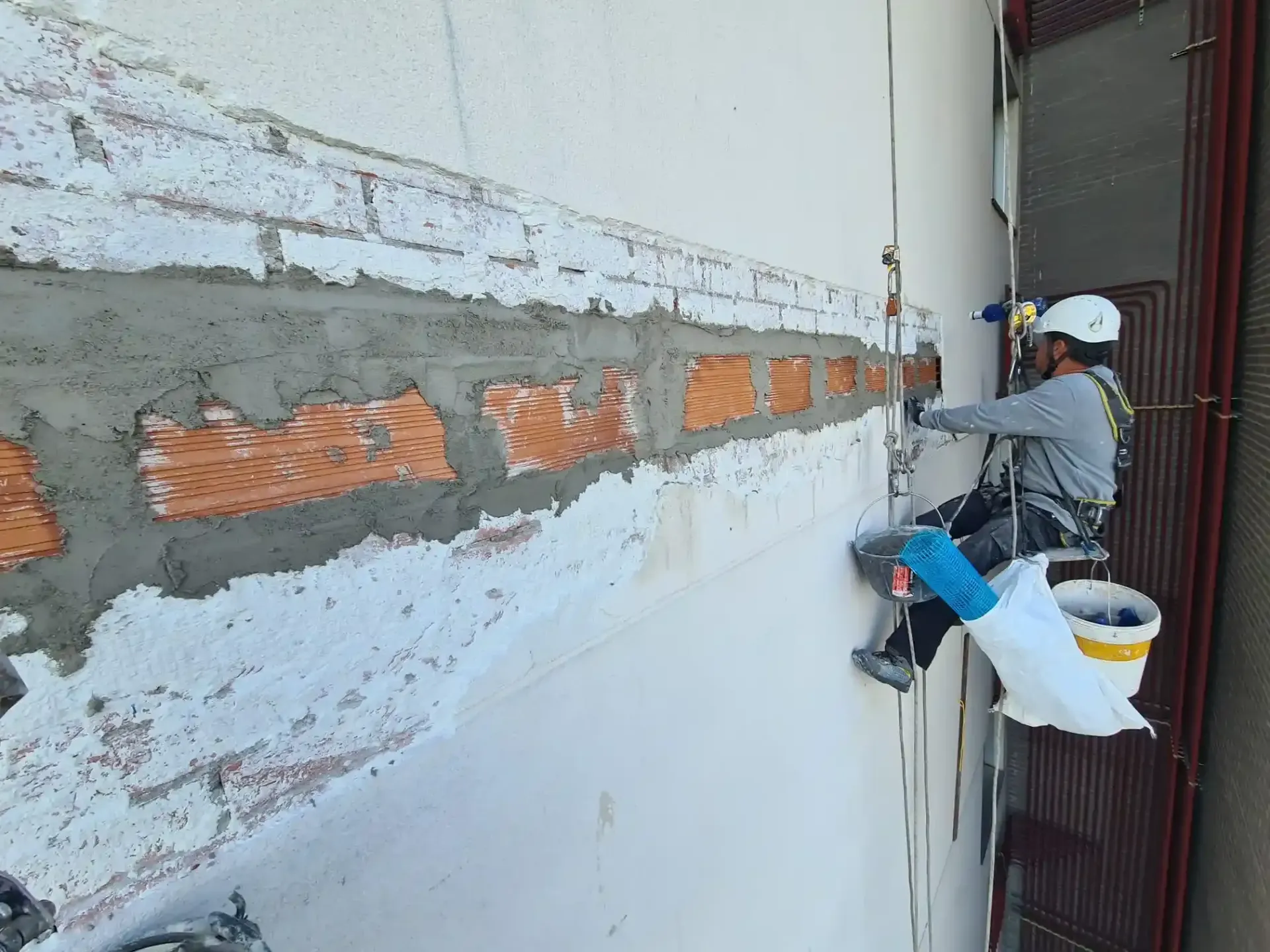 Un trabajador aplica yeso a una pared dañada en una obra de construcción, utilizando una llana y un cubo.