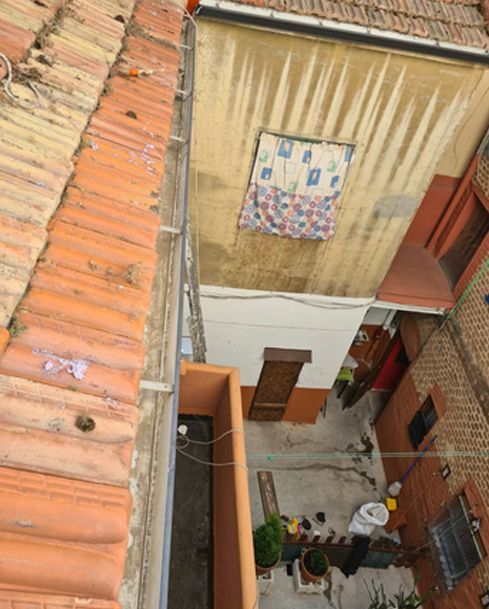 Patio estrecho entre edificios, con dos personas abajo y ropa tendida en una pared beige.