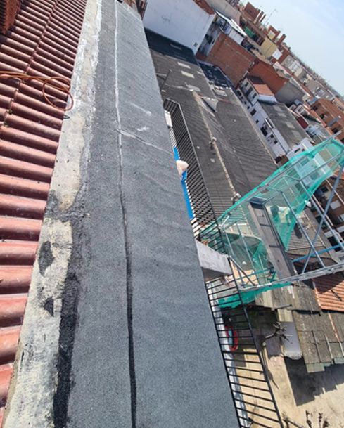 Un trabajador repara una pared agrietada, aplicando yeso desde un cubo mientras está subido a un andamio.